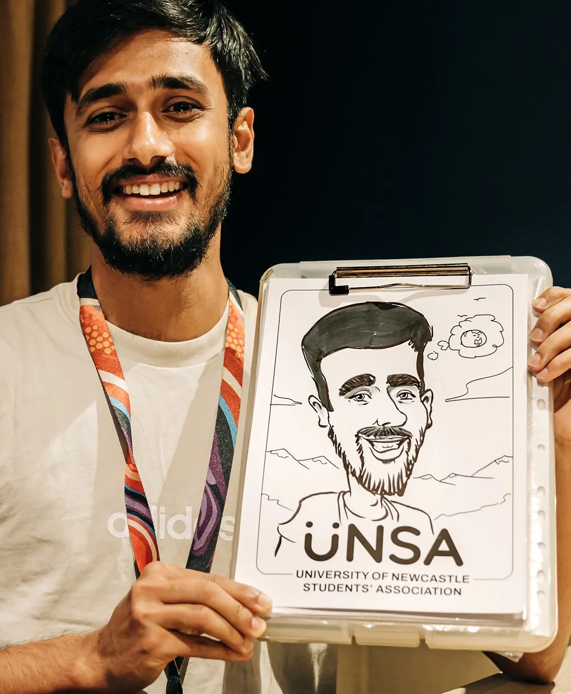 Smiling man holding his caricature, with the UNSA university logo