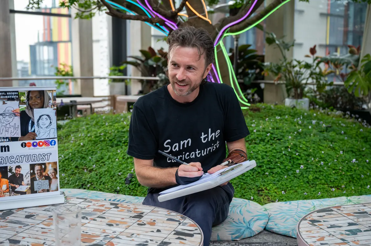 Sam McNair drawing a caricature on a clipboard, smiling up at a guest