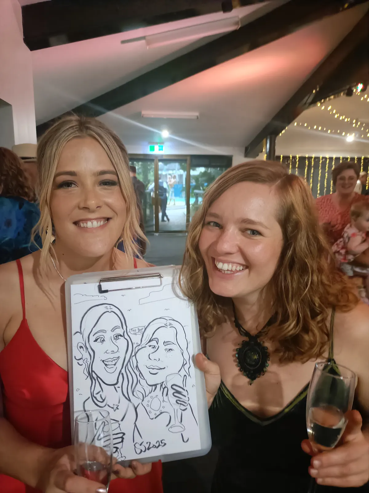 Two women smiling and holding up their caricature